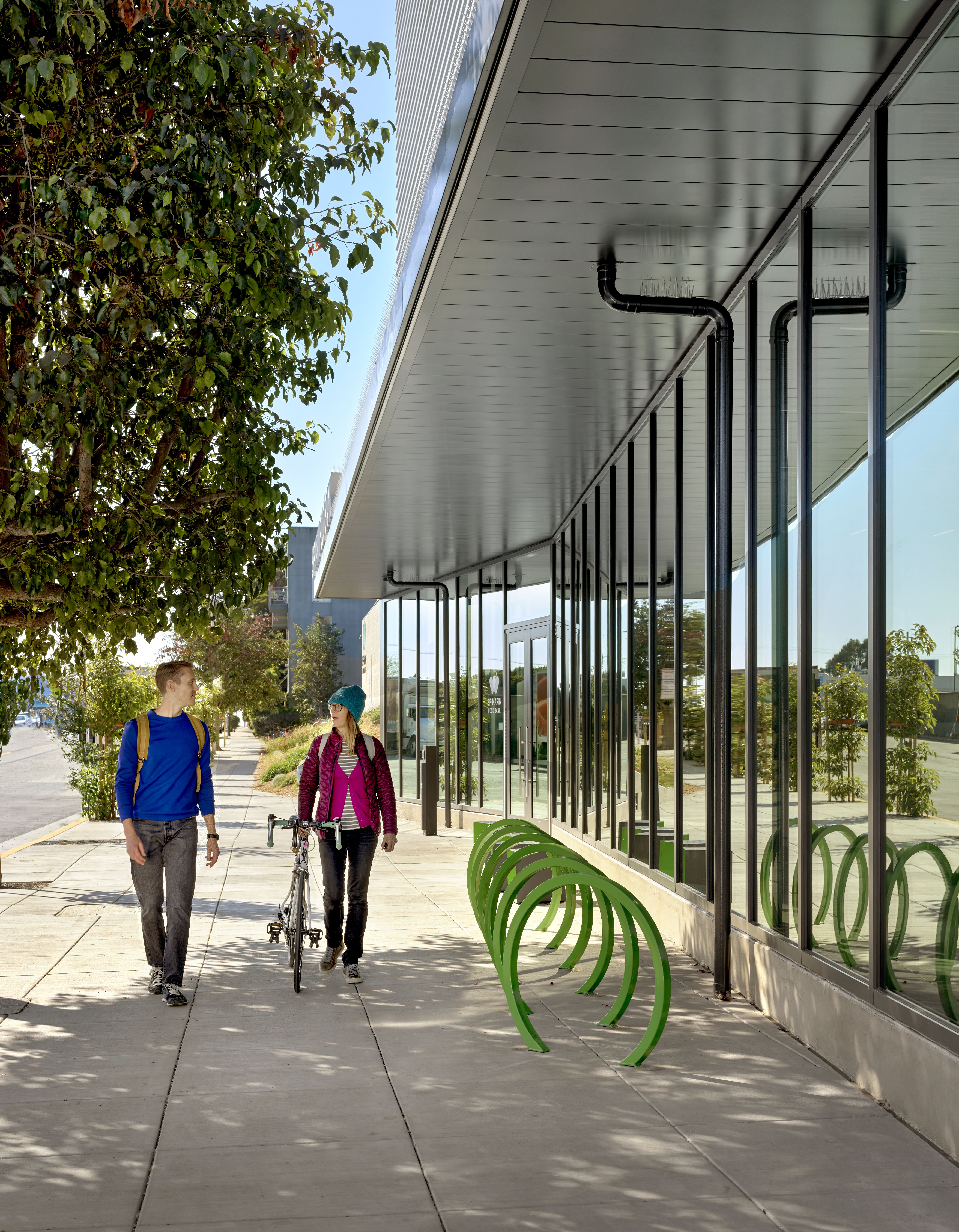 Sidewalk view of people walking with bicycle racks in front of building.