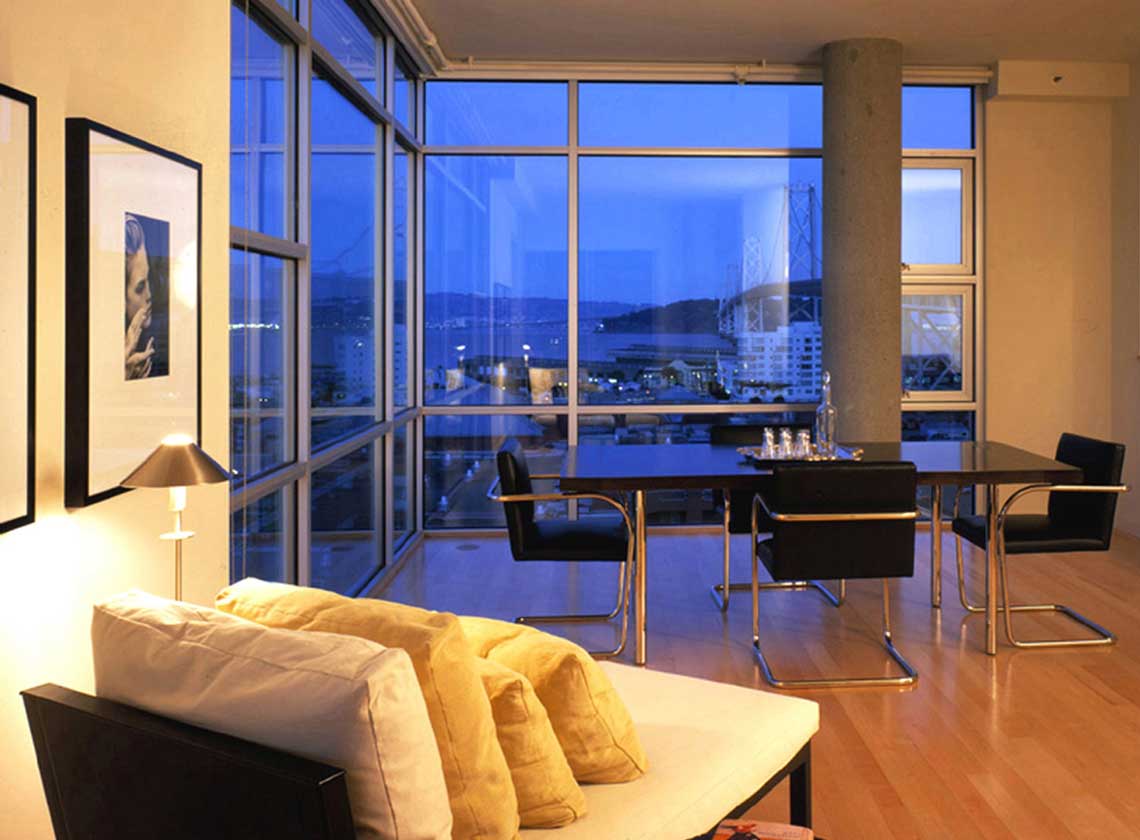 Interior evening view of furnished dining area with views of the Bay Bridge through floor to ceiling windows