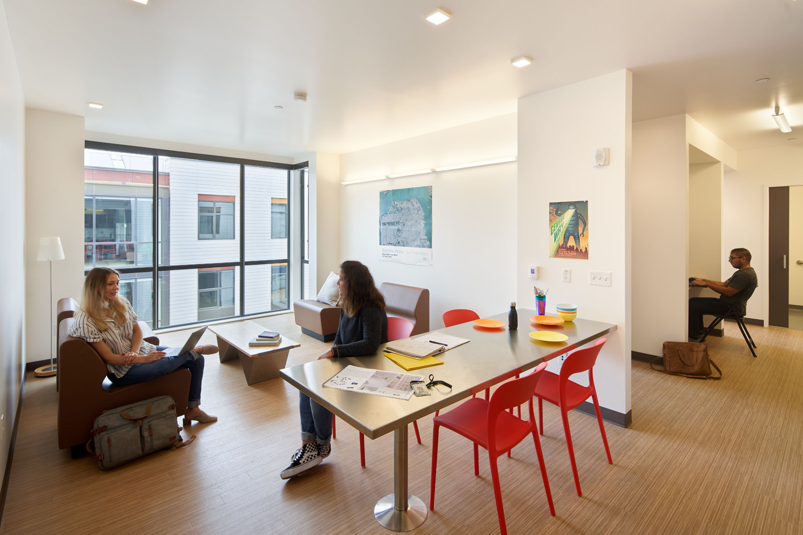 Image of student unit common area living room and desk space with couches, tables, and chairs. 