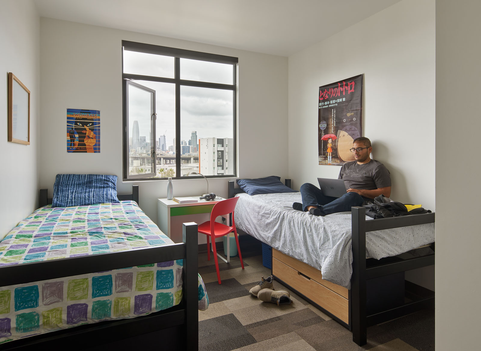 Image of student unit bedroom with two twin beds and desk below the window separating the two