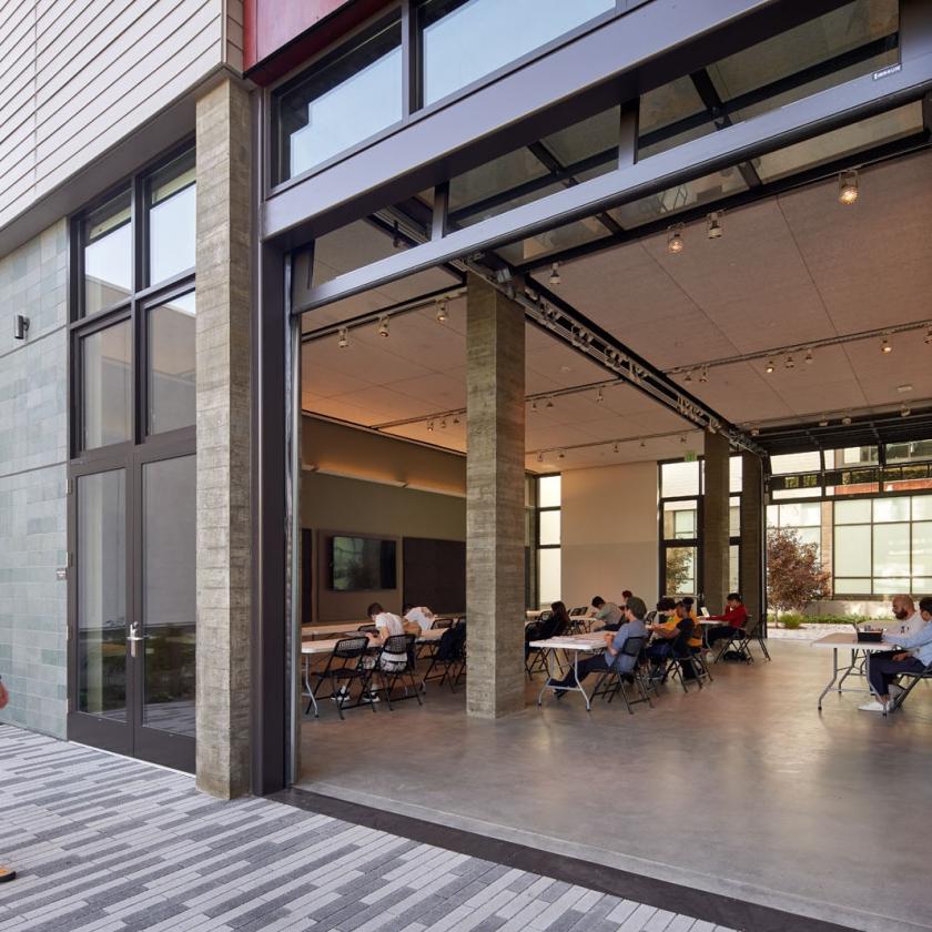 Daytime view looking into a large open modern interior learning space through a retractable garage door