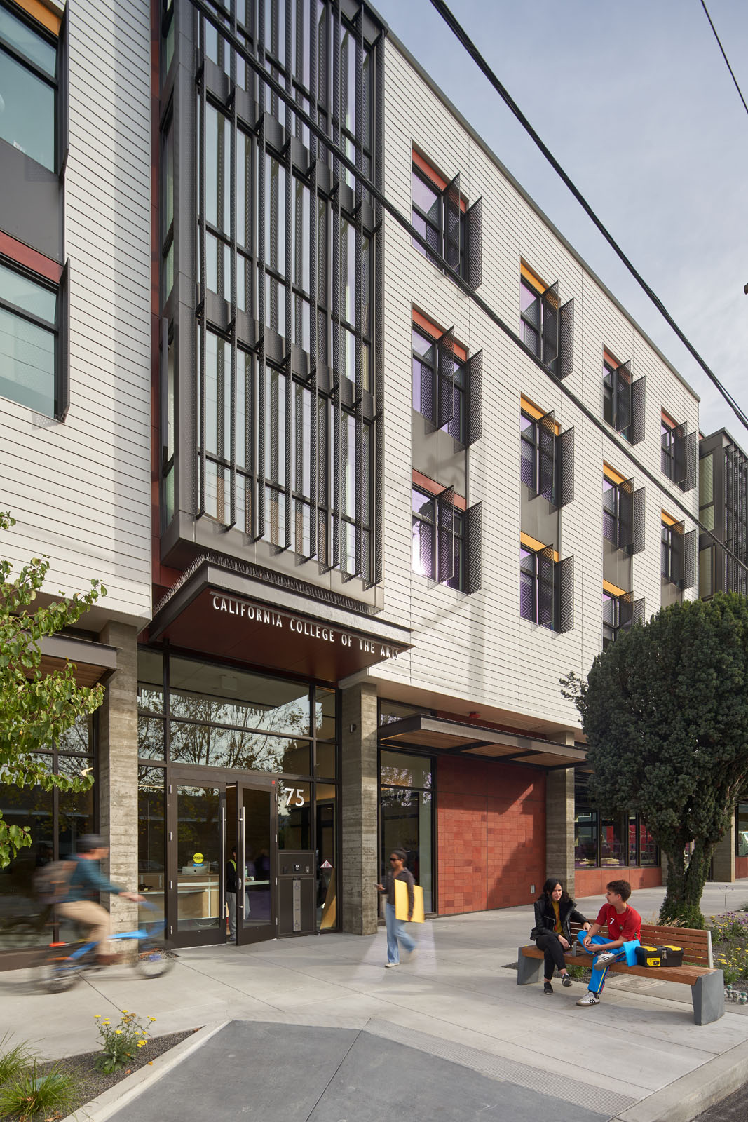 View of entrance of four story building with students seated on bench in front of building.