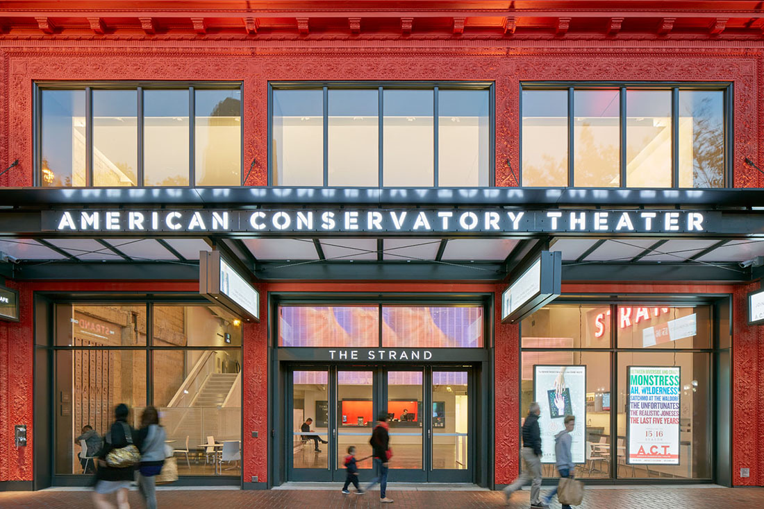 Close view of entry with illuminated American Conservatory Theater sign on overhang; lobby is visible through large windows