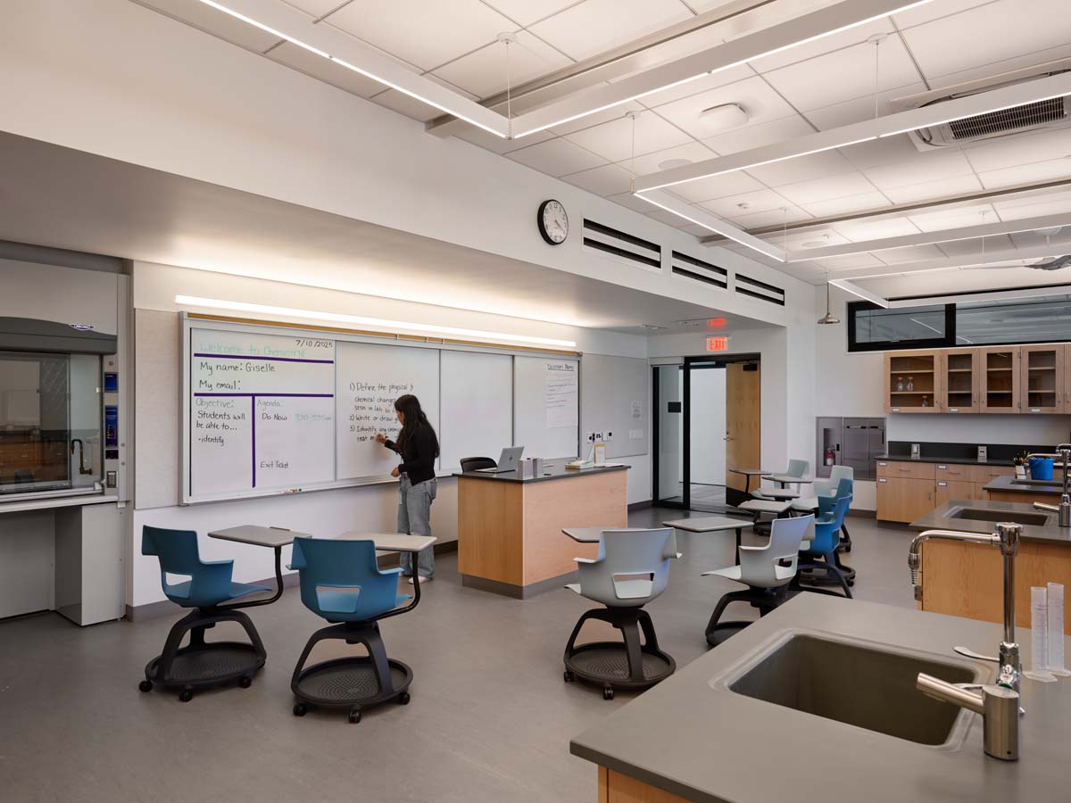 Classroom with teacher at whiteboard and empty desks.