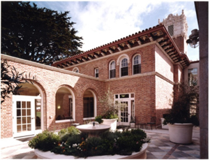 View of courtyard with fountain in foreground and historic brick building with arches behind.