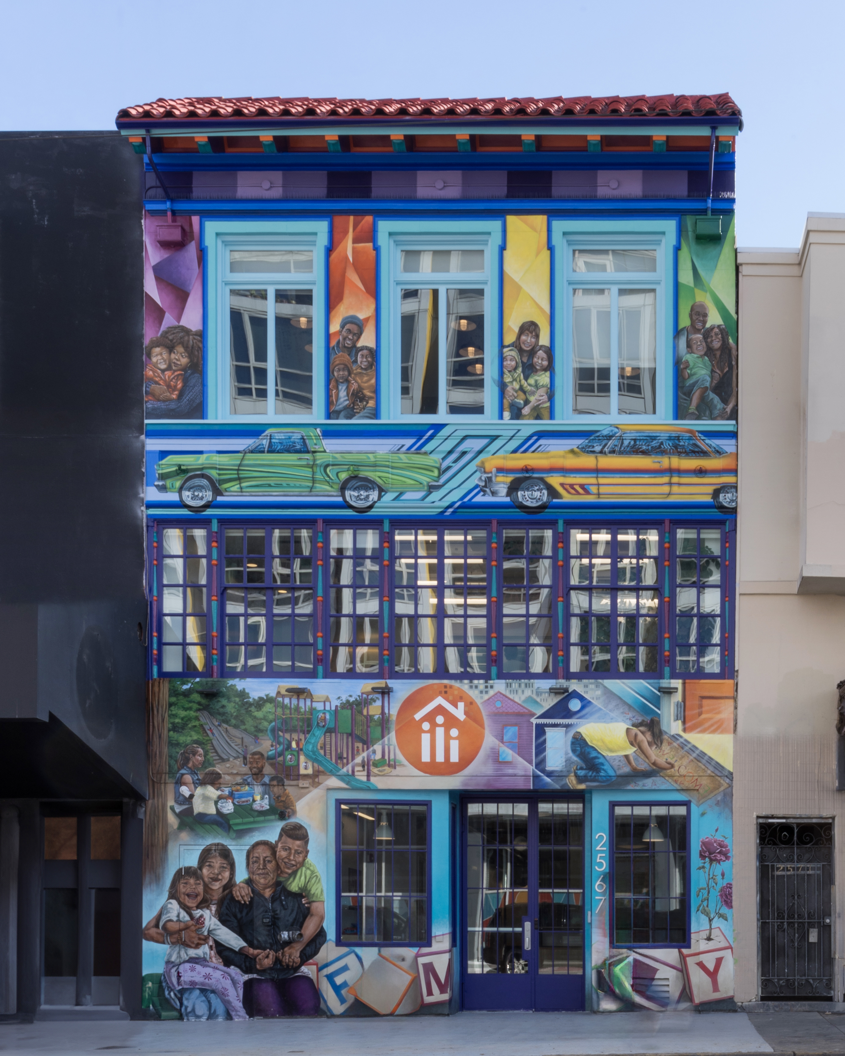 Four story building with a multi-colored mural painted on entire front facade depicting families.