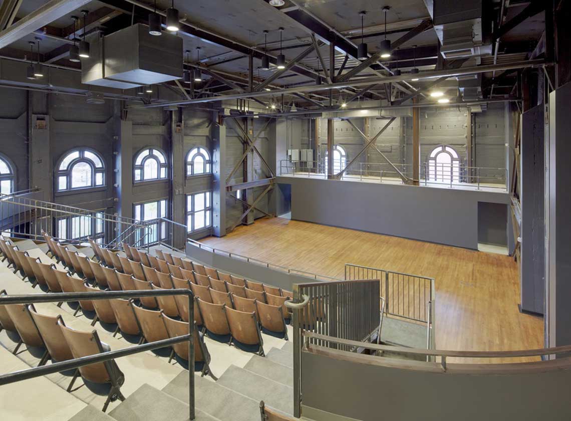 Performance space as viewed from top row of balcony with large arched windows and exposed concrete structure