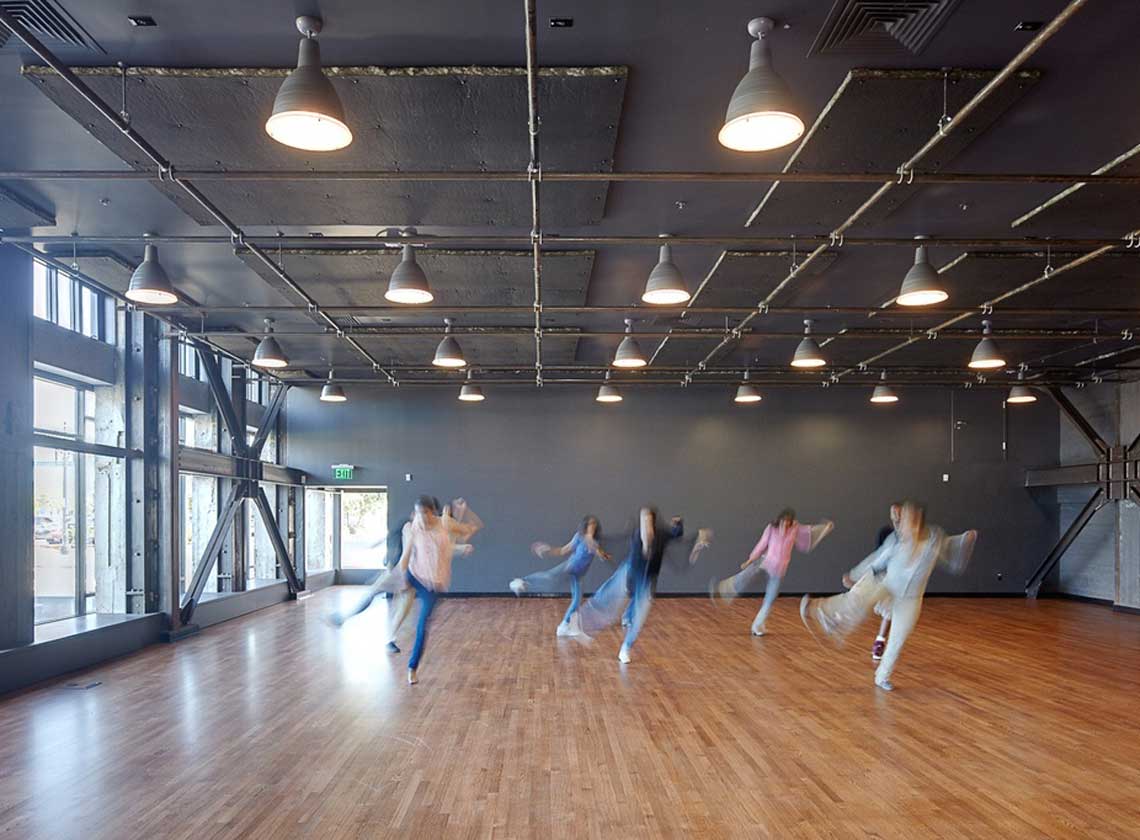 Young people in motion practicing a dance routine in a brightly-lit rehearsal space