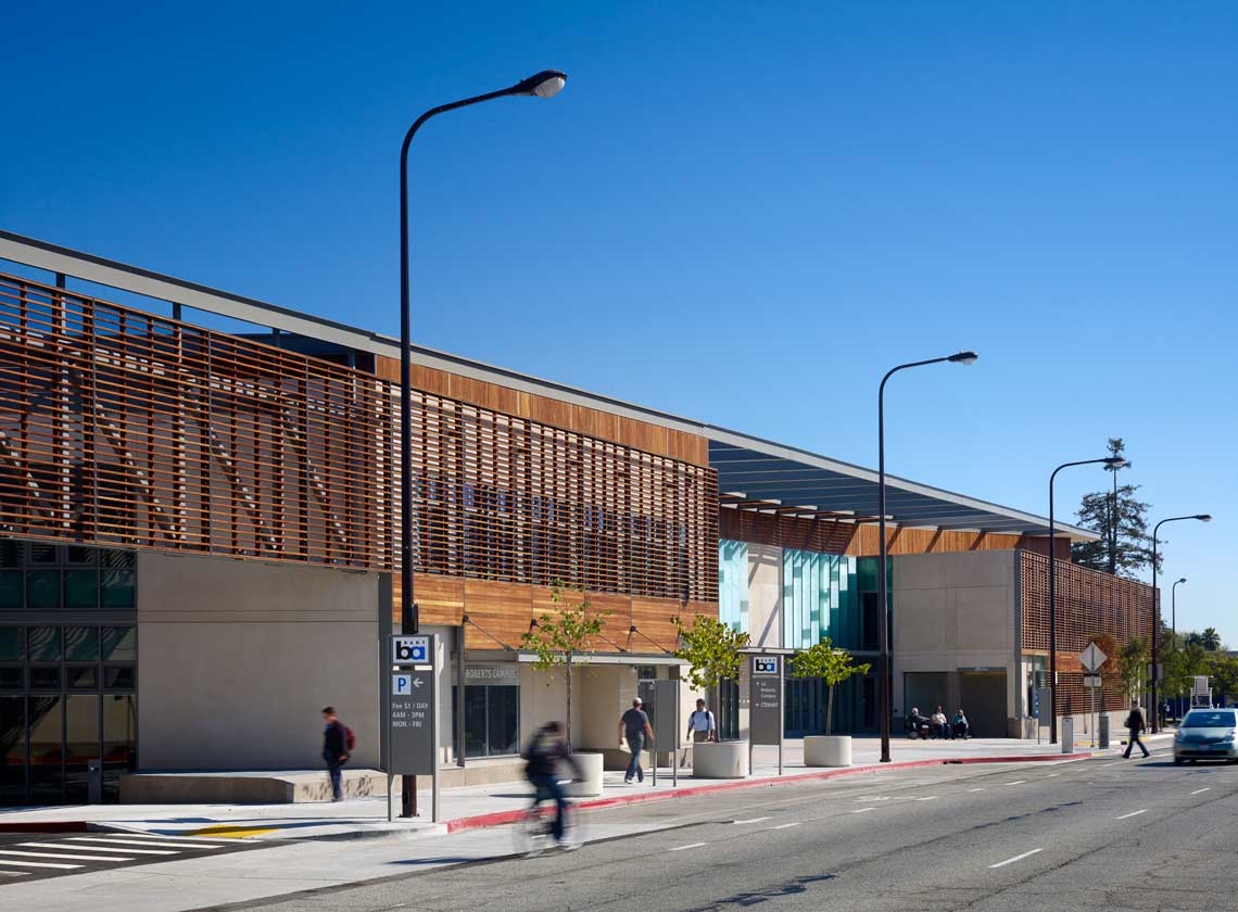 Building façade with modern wooden slat details along Adeline Street; BART entrance and parking signs along the sidewalk.