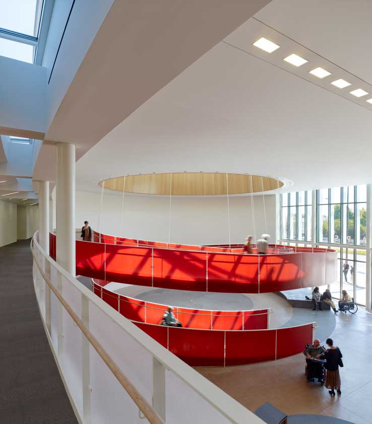 Interior view of lobby with bold red accessible spiral ramp as seen from a second-floor corridor