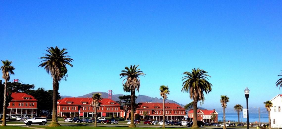 View of lawn and main post in the Presidio of San Francisco with brick buildings nad Golden Gate Bridge in background.