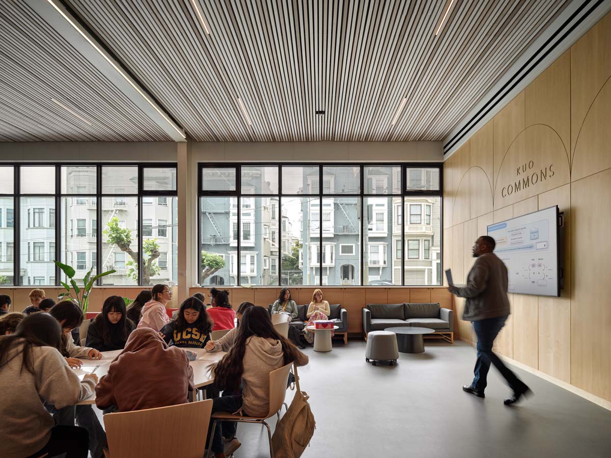 Classroom with students seated at round tables and teacher standing at whiteboard.