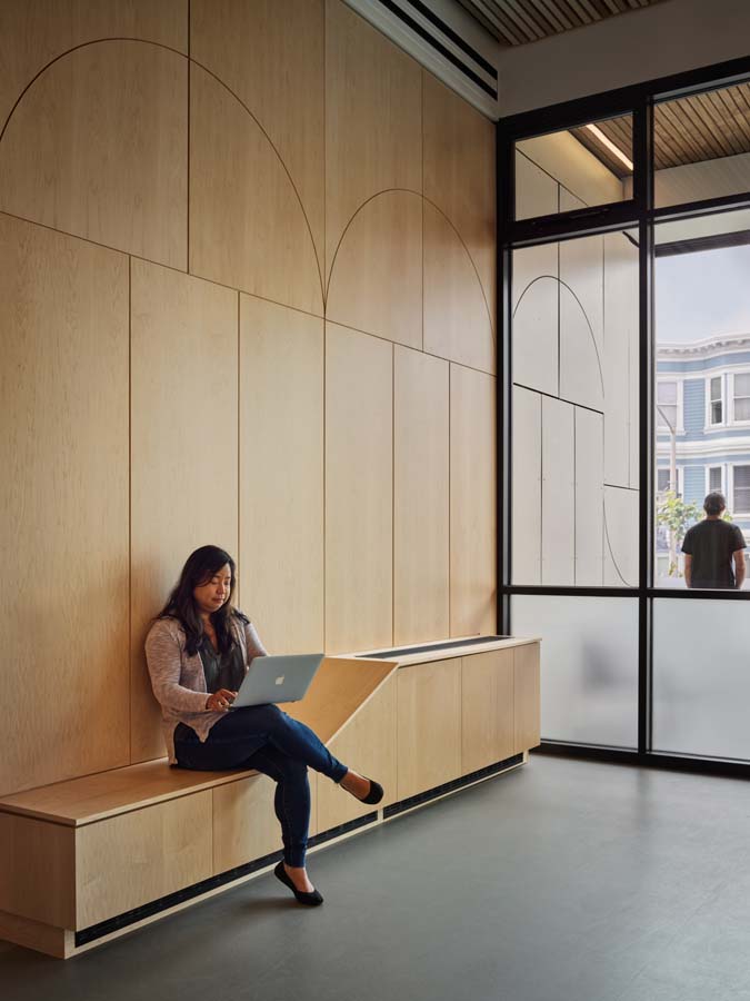 Student seated on common area bench near windows.
