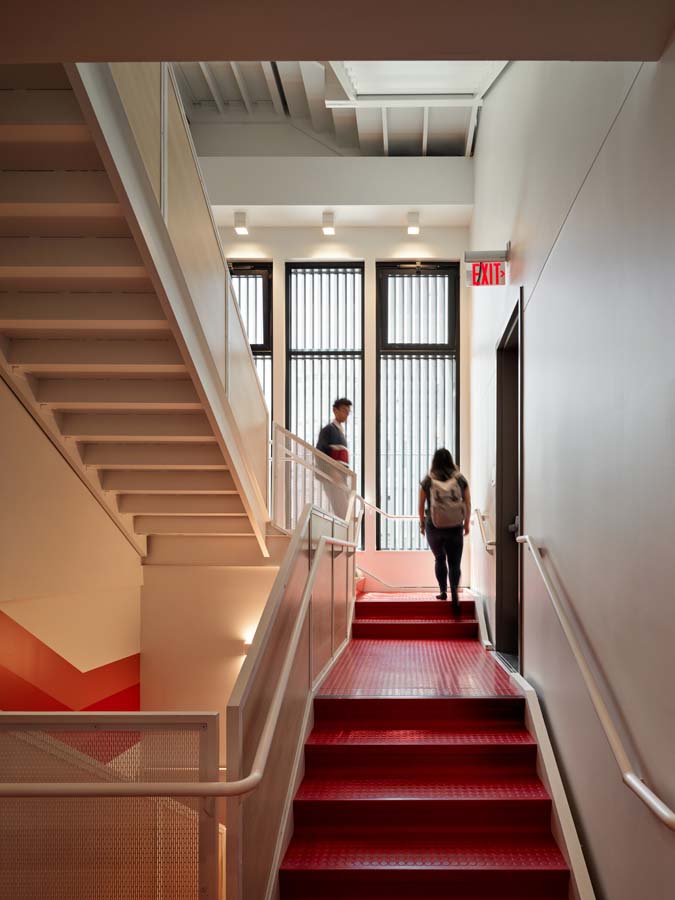 Interior staircase with red floors and steps with white walls and railings.