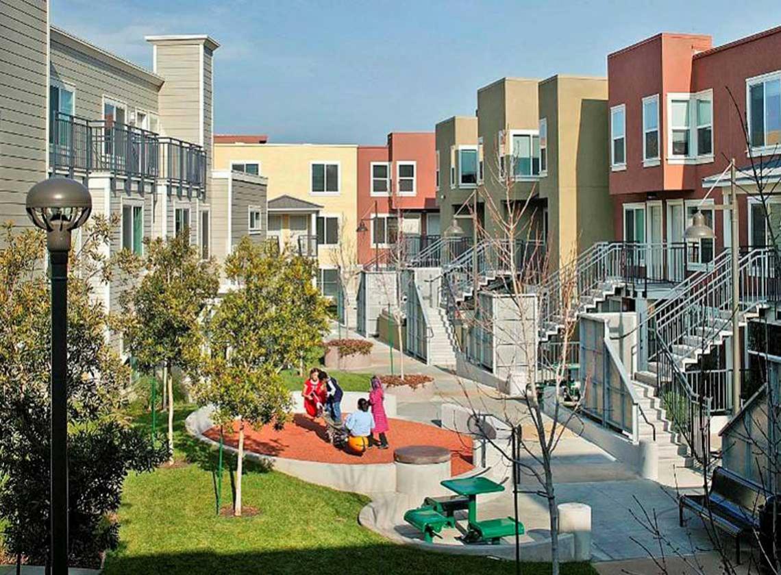 Colorful exterior walls of multifamily units facing a landscaped courtyard with picnic table and play area