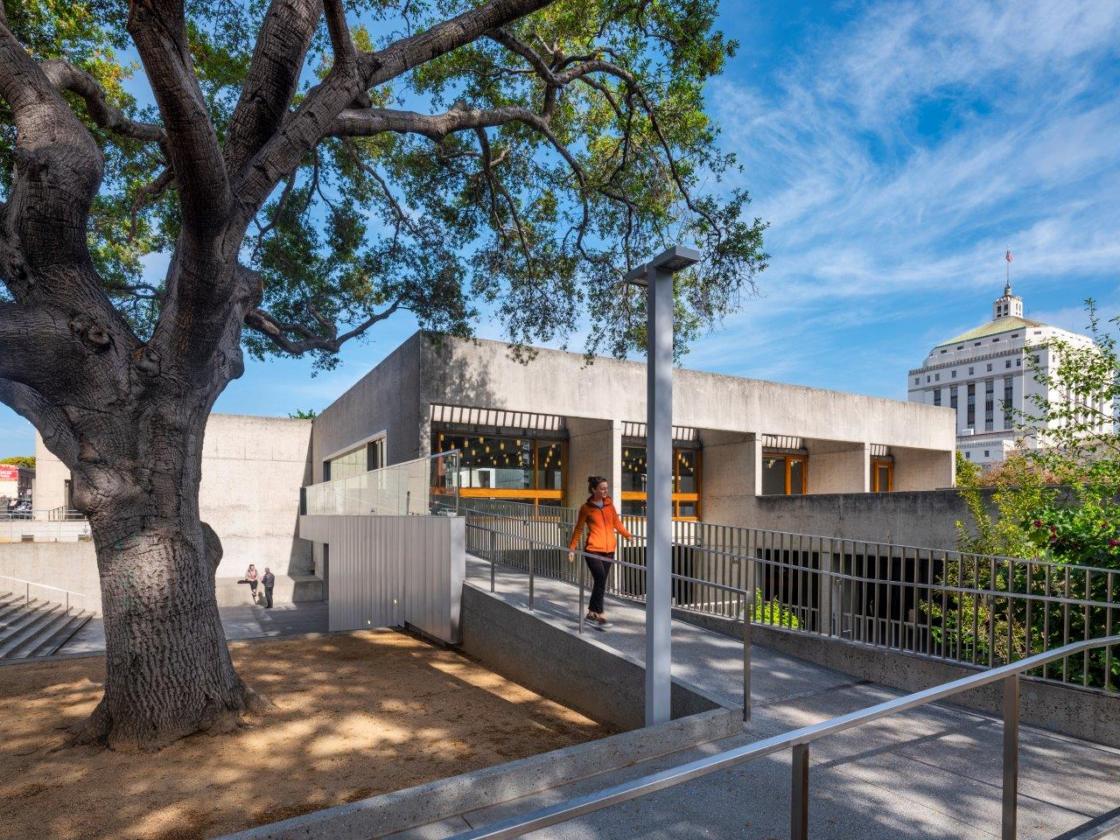 Museum exterior and tree with person walking by.