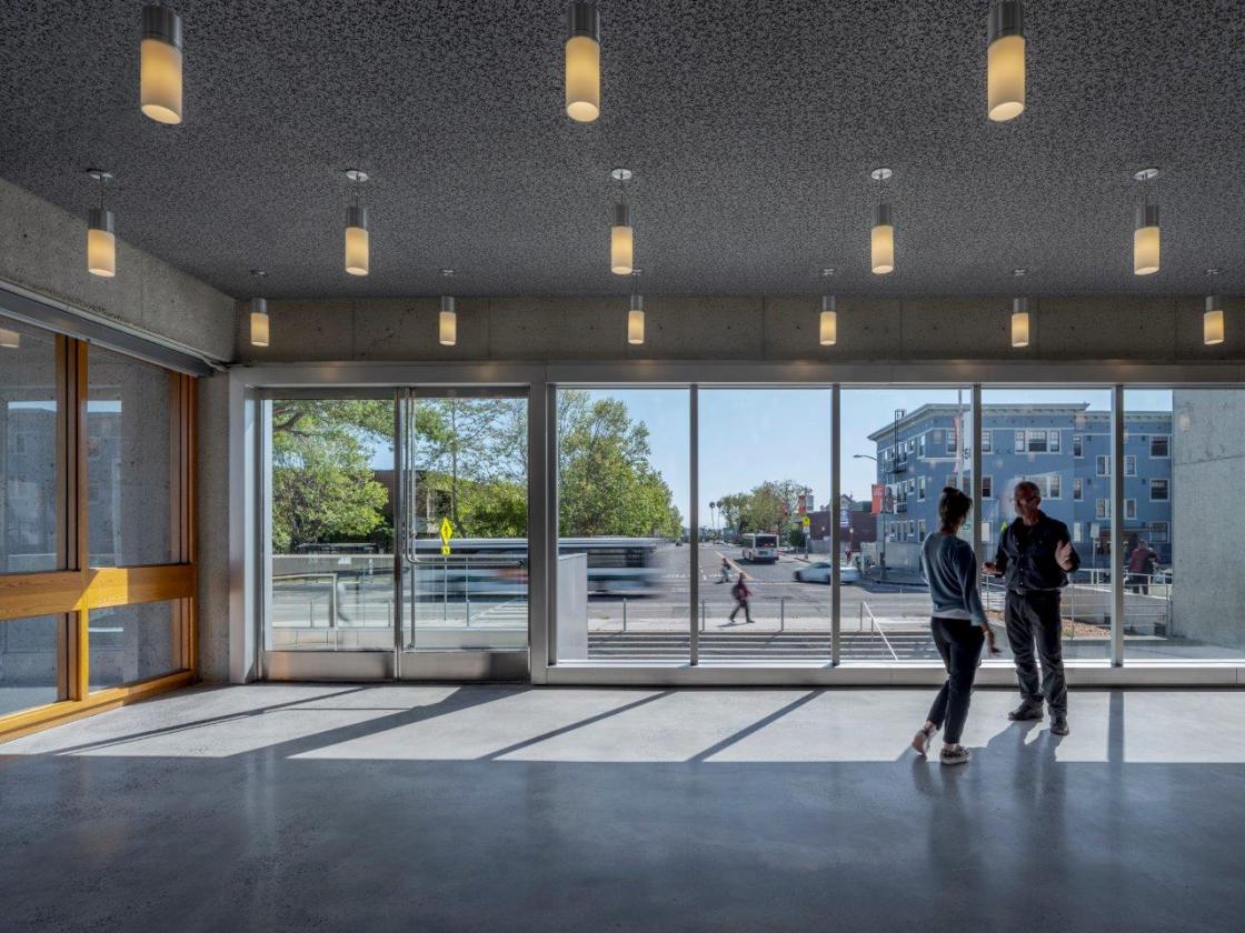 Museum interior with people looking out floor to ceiling windows to terrace and city..