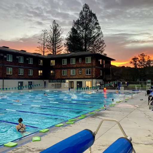 Exterior of pool showing divided swimming lanes with building in background at sunset