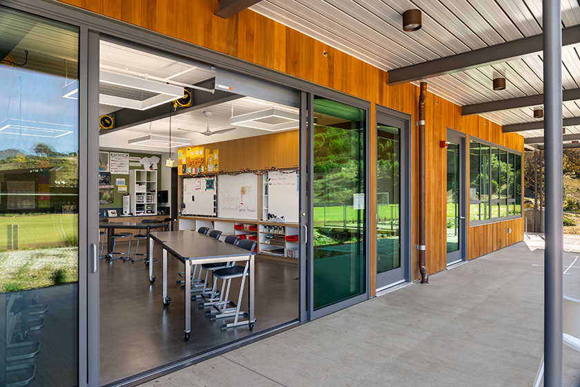 Exterior view looking into classroom through large sliding glass walls, connecting classroom to nature