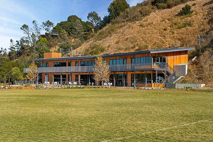 Exterior daytime view of school building nestled into a hill, as seen from across a large grass field