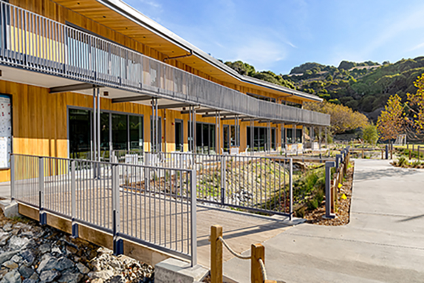 Daytime view of building exterior with wood siding and second-floor walkway railing in natural outdoor setting