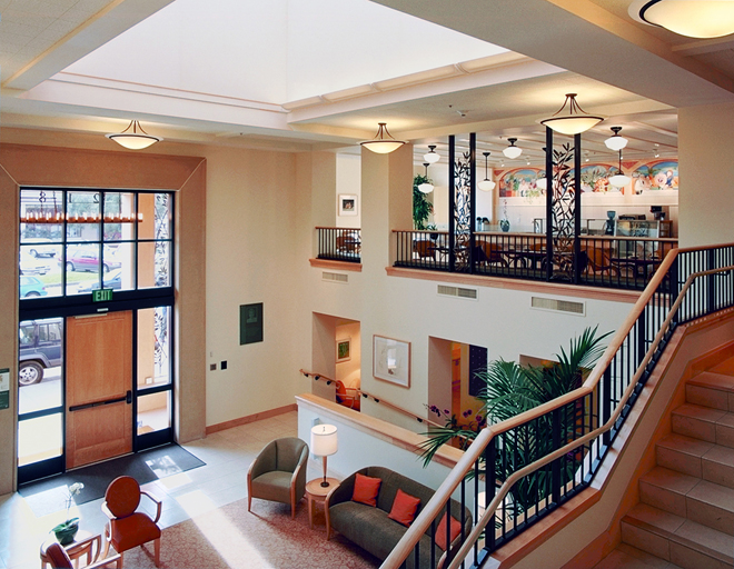 Interior view of entrance lobby with seating areas and double-height ceiling and staircase to cafe