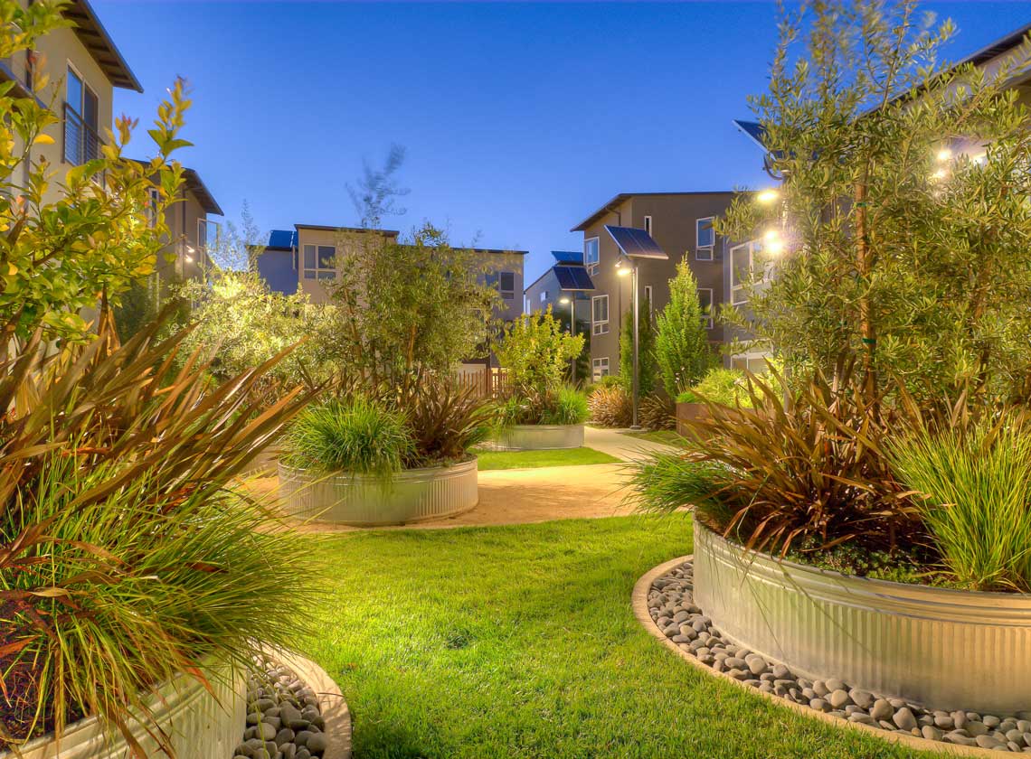 Detail of exterior courtyard landscaping with large round metal planters and lawn at dusk