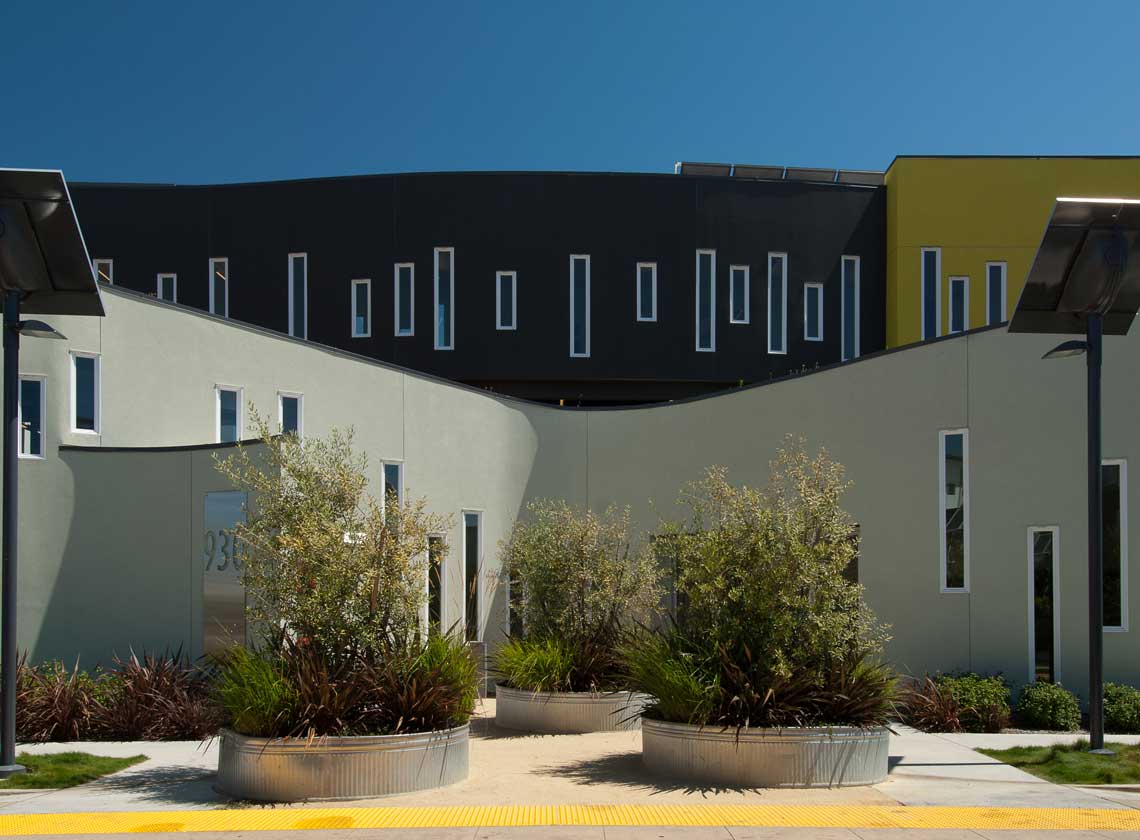 Exterior view of curving architectural walls with slim windows at staggered heights, large planters in the foreground