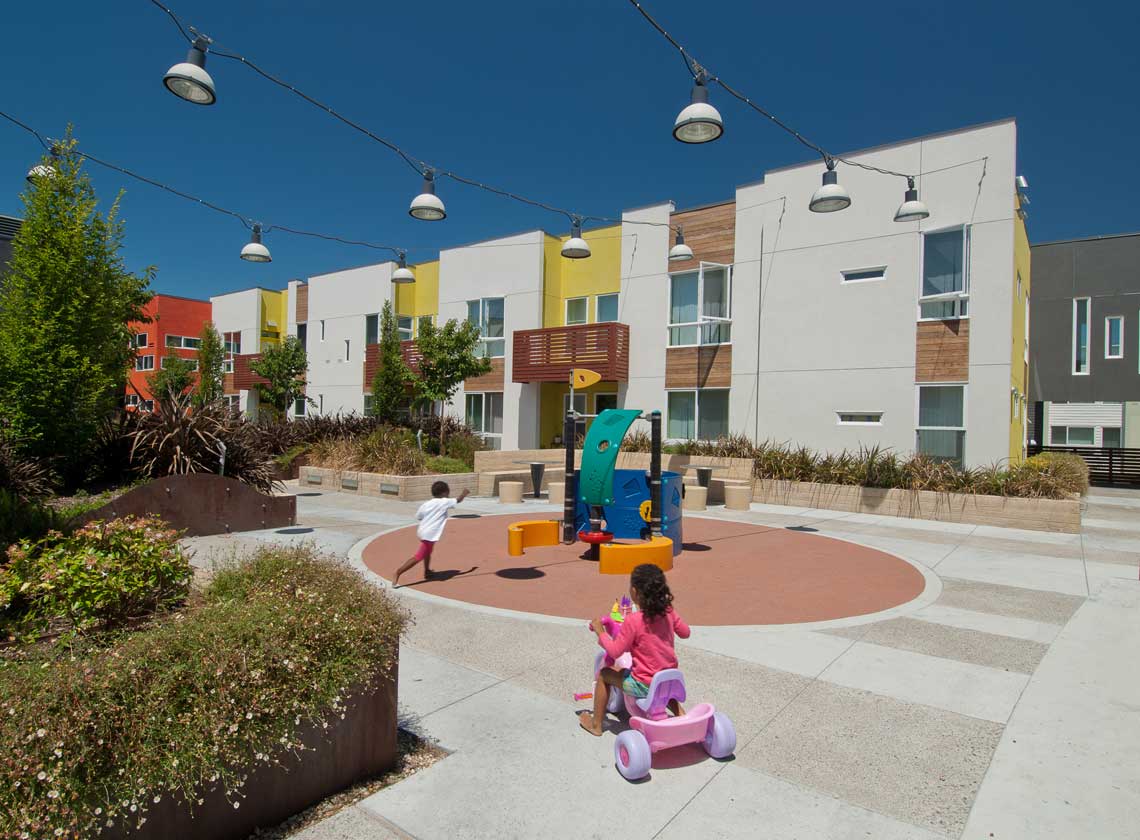 Exterior daytime view of landscaped courtyard with children in a play area under strings of hanging down lights