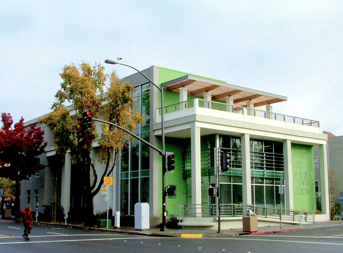 Exterior daytime corner view of three-floor building with bright green accents, bold graphic signage, and columns