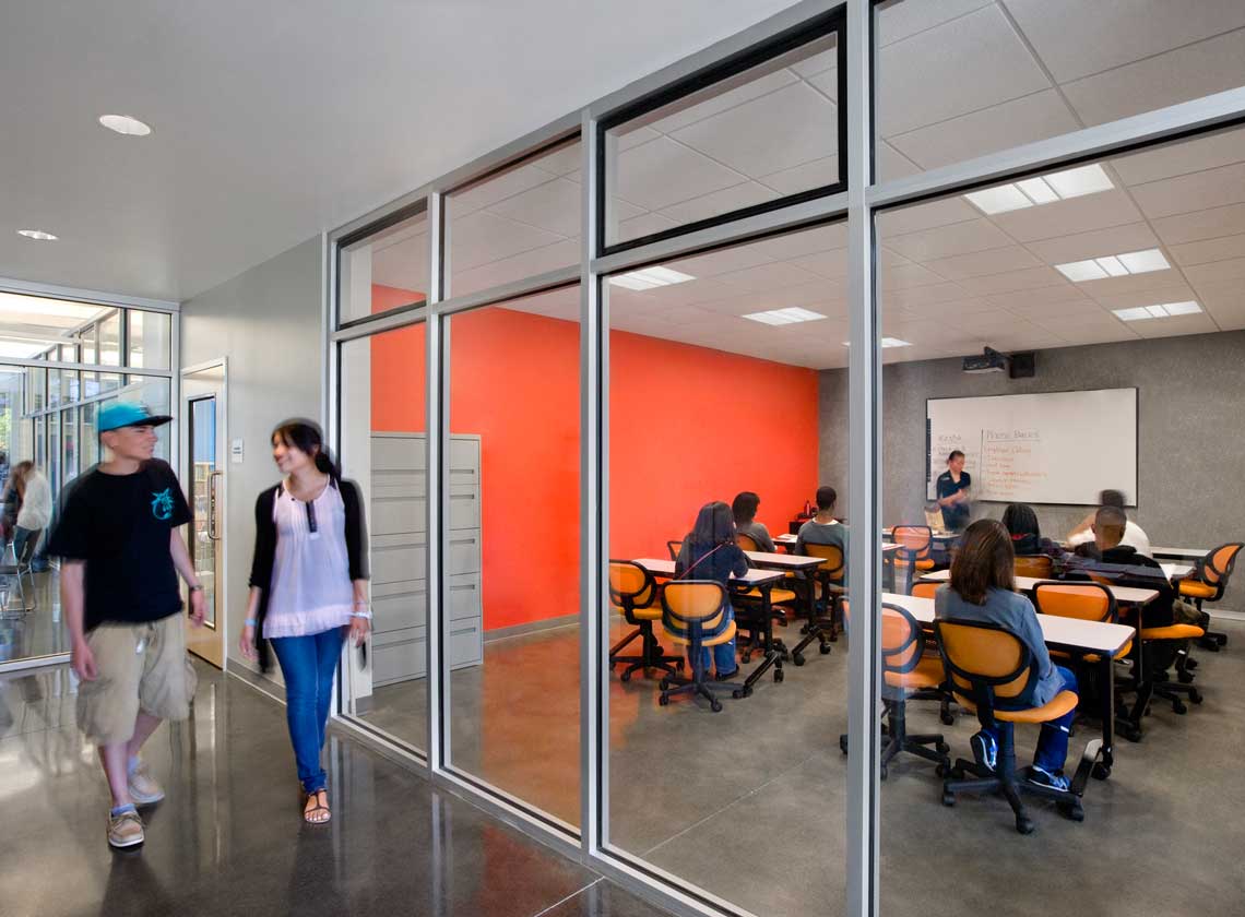 Interior view of hallway and classroom through glass walls; students at tables attending a lecture