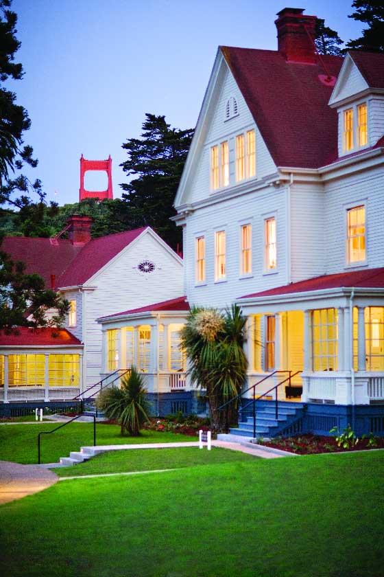 Evening view of a lodge building illuminated from inside with top of Golden Gate Bridge in the distance.