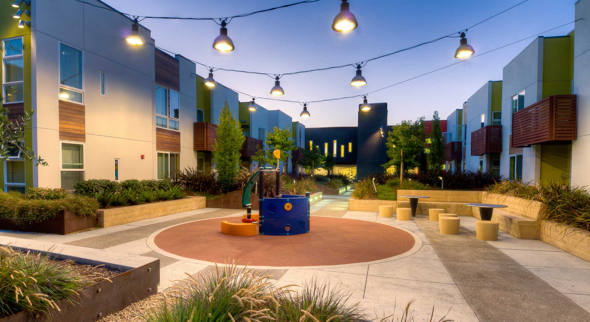 Evening view of a courtyard at Tassafaronga Village with playground between multifamily buildings