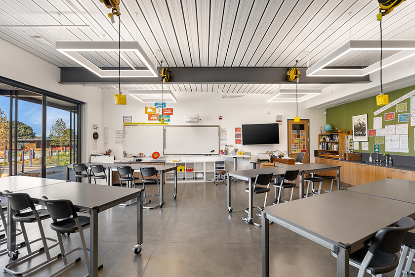 Interior view of classroom lab space with high tables and chairs; window walls open to outdoors