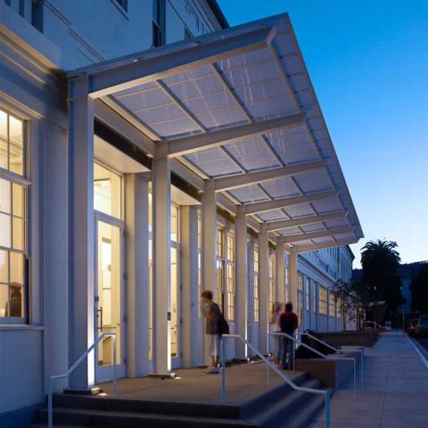 Exterior evening view of building with modern renovated entry overhang; interior lighting visible through large windows