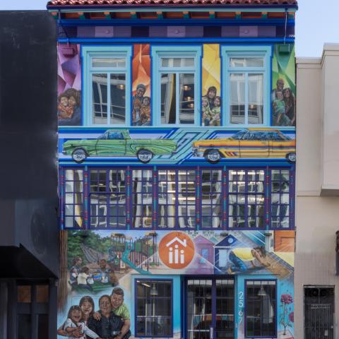 Image of three story building painted with a mural depicting families.