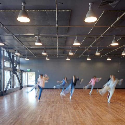 Young people in motion practicing a dance routine in a brightly-lit rehearsal space