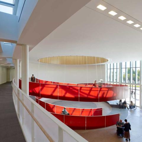 Interior view of lobby with bold red accessible spiral ramp as seen from a second-floor corridor