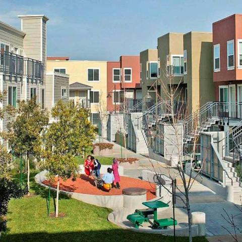 Colorful exterior walls of multifamily units facing a landscaped courtyard with picnic table and play area