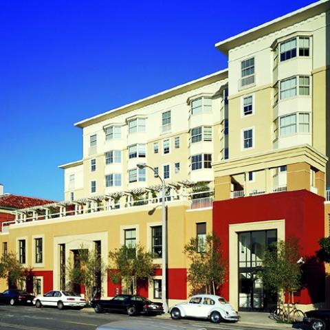 Exterior daytime view of community including multi-story living units and terrace above a two-floor pedestal and entryway