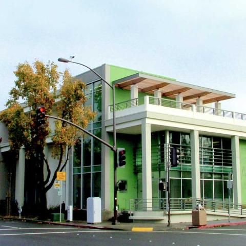 Exterior daytime corner view of three-floor building with bright green accents, bold graphic signage, and columns