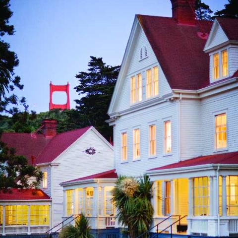Evening view of a lodge building illuminated from inside with top of Golden Gate Bridge in the distance.