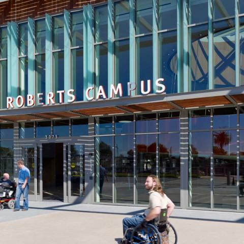 Exterior daytime view of building entrance with "Ed Roberts Campus" sign in large letters. People coming and going including two