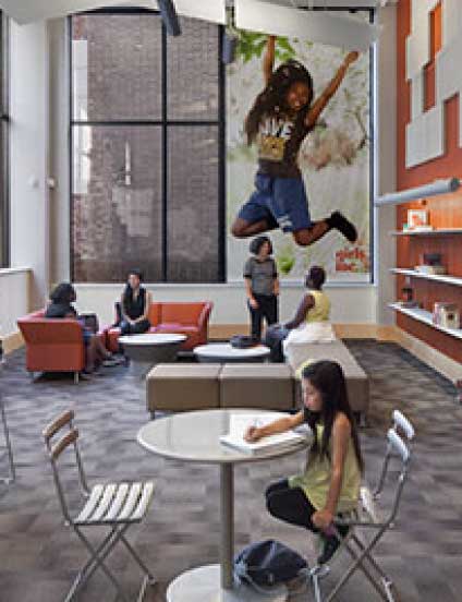 Spacious interior lounge with women and girls seated playing and talking at the Girls Incorporated of Alameda County facility.